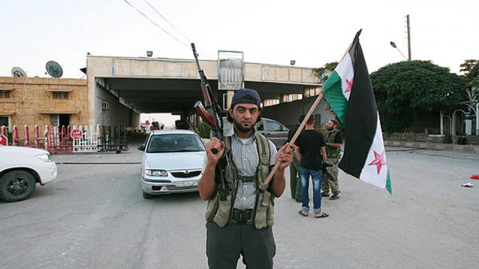 A Free Syrian Army soldier holds a rifle and a Syrian flag at the Bab al-Salam border crossing to Turkey on July 22, 2012.