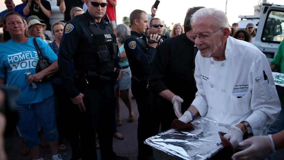 FORT LAUDERDALE, FL - NOVEMBER 12: A Fort Lauderdale Police Officer watches as Arnold Abbott, a 90-year-old chef, carries food to be dished out to the homeless in violation of a recently passed city law on November 12, 2014 in Fort Lauderdale, Florida.